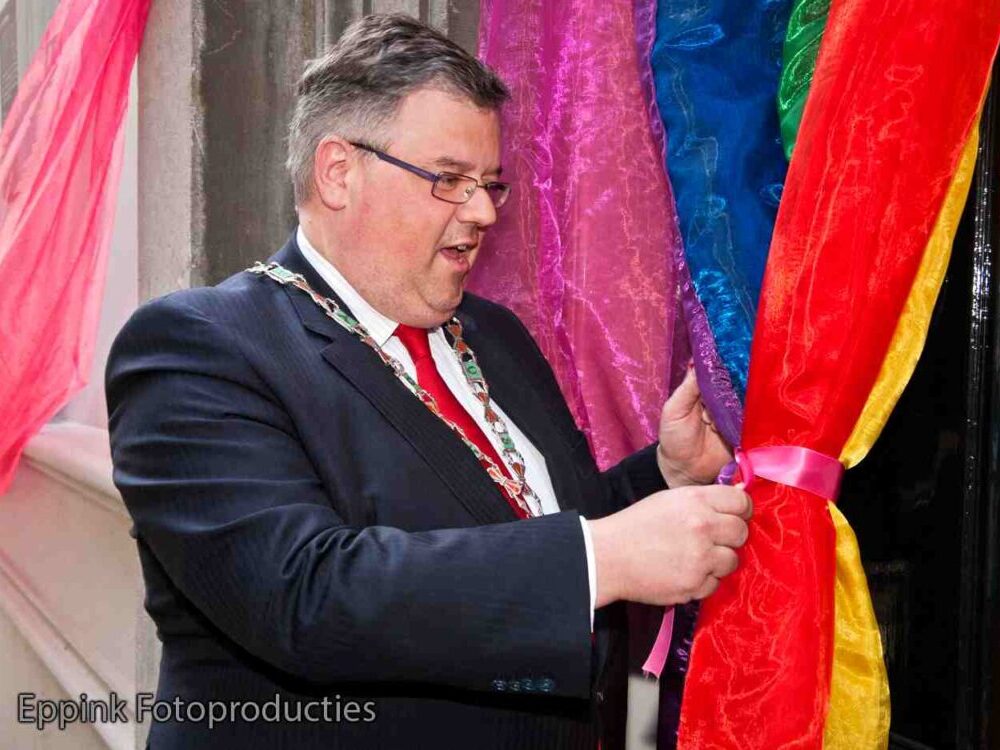 Burgemeester Bruls heeft een roze strik vast bij de opening van het Roze Huis